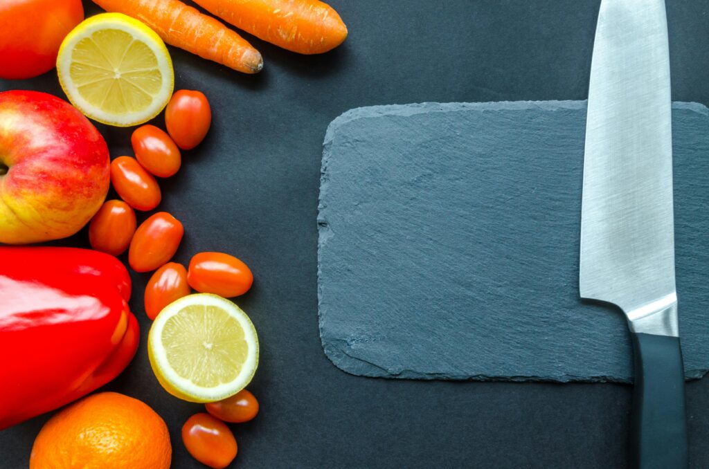 pexels-photo-952479-952479 Vibrant fruits and vegetables with a stainless steel knife on slate, perfect for healthy eating concepts.